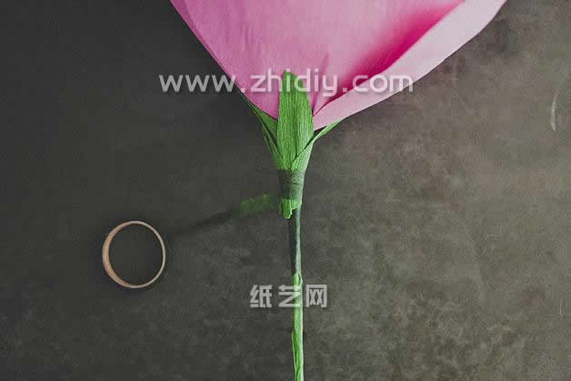 第十二步是将缠绕到纸玫瑰花瓣下方的纸花萼用纸胶带进行缠绕，从而固定花萼，使得纸玫瑰看起来更加的漂亮
