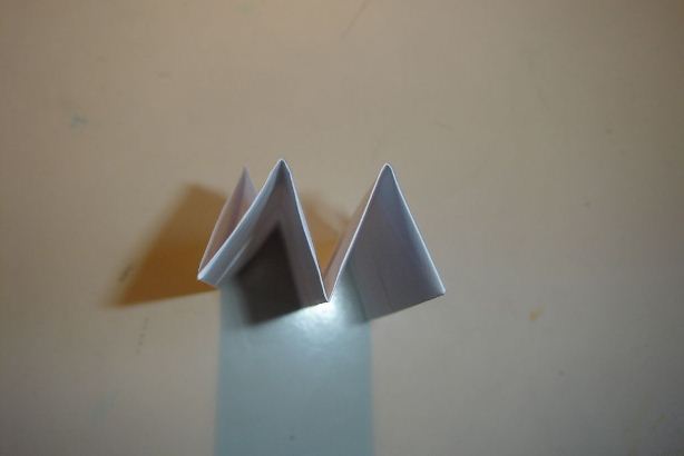 现在在前一步的基础上继续将折纸模型的左右两个顶角向下进行翻折，这样得到的手工折纸船后面的结构