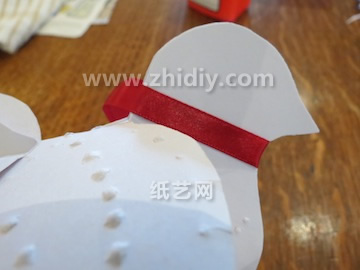 将红色的丝带缠绕到圣诞白鸽的脖颈上之后这个简单的圣诞节纸艺吊饰白鸽就制作完成了