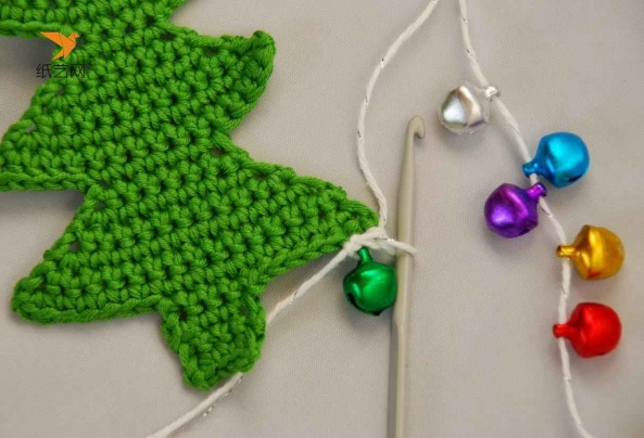 下面用白色的毛线，穿上彩色的小铃铛，然后用钩针在圣诞树下面一层上开始钩边