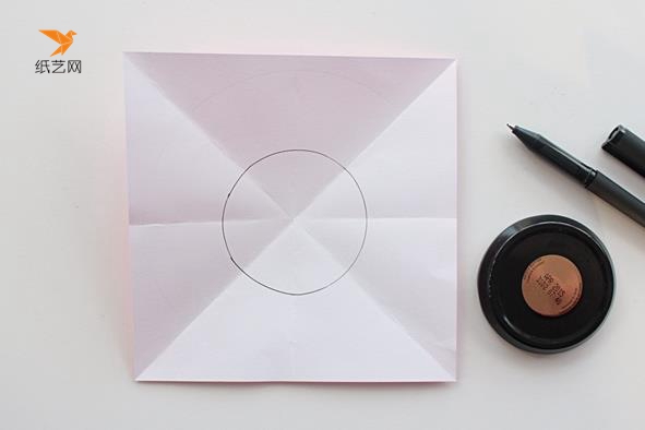 将这个正方形的纸对角对边对折之后，打开，在中间画上一个小的圆形