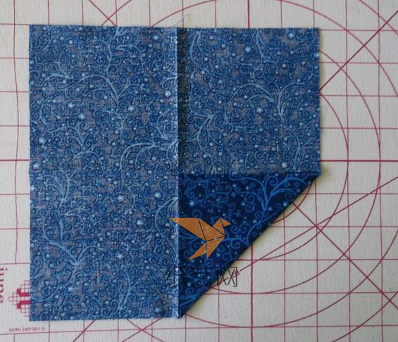 把正方形的布背面朝上，对边对折之后，将角折到中间交点的位置