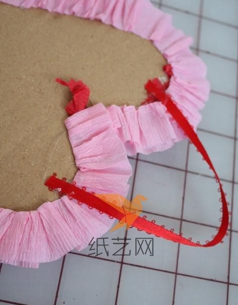用粉色的皱纹纸折叠的一边粘到心形的边缘，就成为花边了，然后在上面固定好丝带方便挂起来