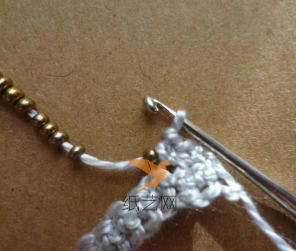 先编织两个短针，接下来就把一颗珠子移到最靠近钩针的位置，编织下一个短针的时候就可以把这颗珠子固定到手链上面了